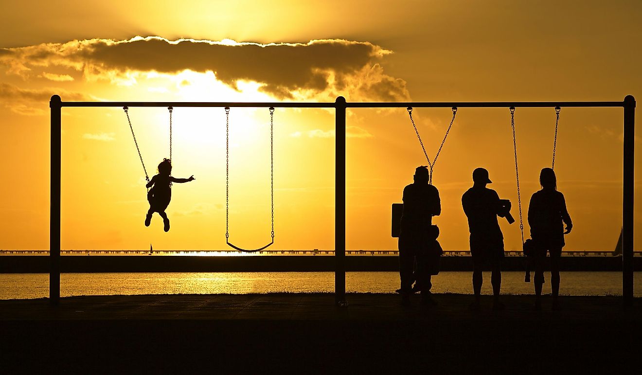 Mandeville, Louisiana: Families in silhouette play on the swings overlooking Lake Pontchartrain at sunset