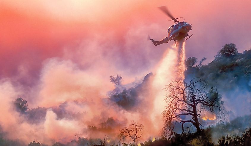 A helicopter dropping water on a California wildfire in rugged terrain