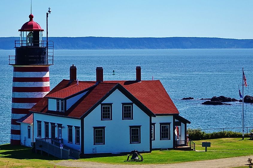 Beautiful view of red & white striped West Quoddy Lighthouse and adjacent keeper's building at a state park in Lubec, Maine, easternmost point in US, with the Atlantic Ocean & blue sky in background.