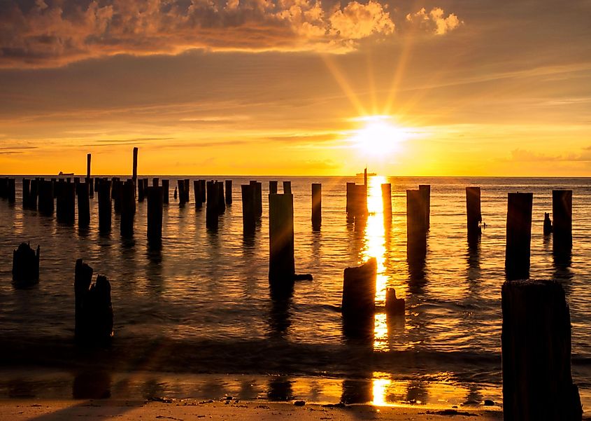 A ship crosses under the sun making a cross with the posts from an old ferry dock during sunset at Cape Charles Virginia in the Chesapeake Bay.