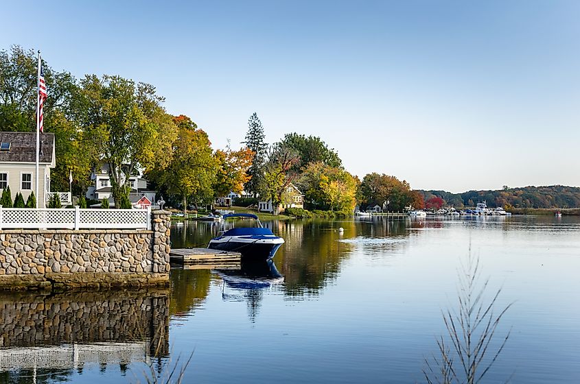 Essex, Connecticut: Waterside houses among trees with boats moored to wooden jetties on a clear autumn day along the Connecticut River.
