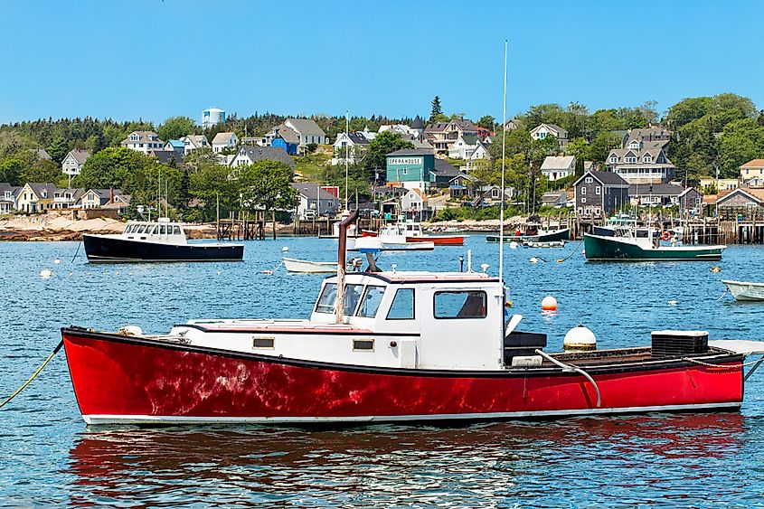 Harbor at Stonington, Maine, USA, features a vibrant red lobster boat in the foreground surrounded by scenic coastal beauty.